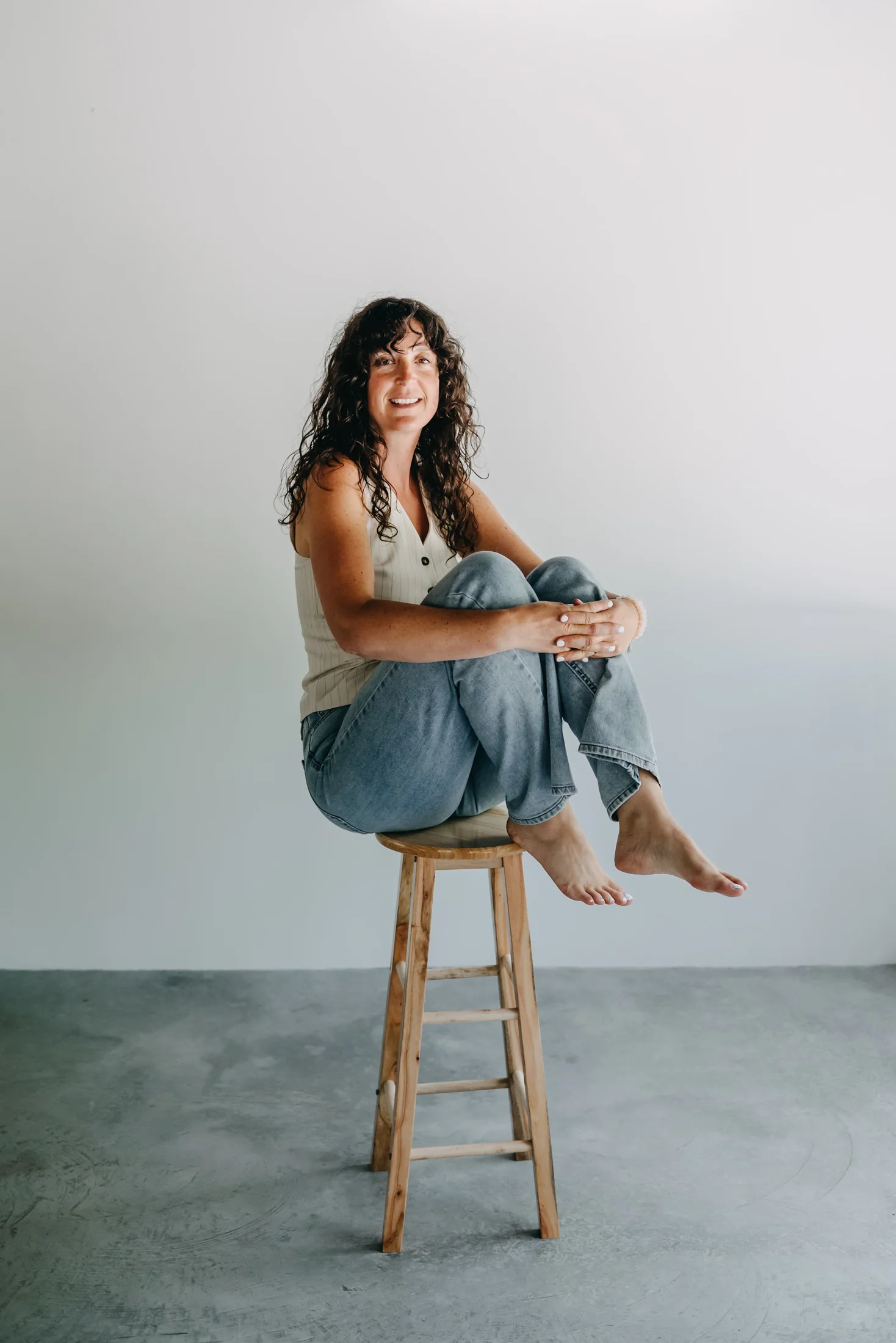 Shelby seated on a stool with her knees drawn in, quiet and thoughtful