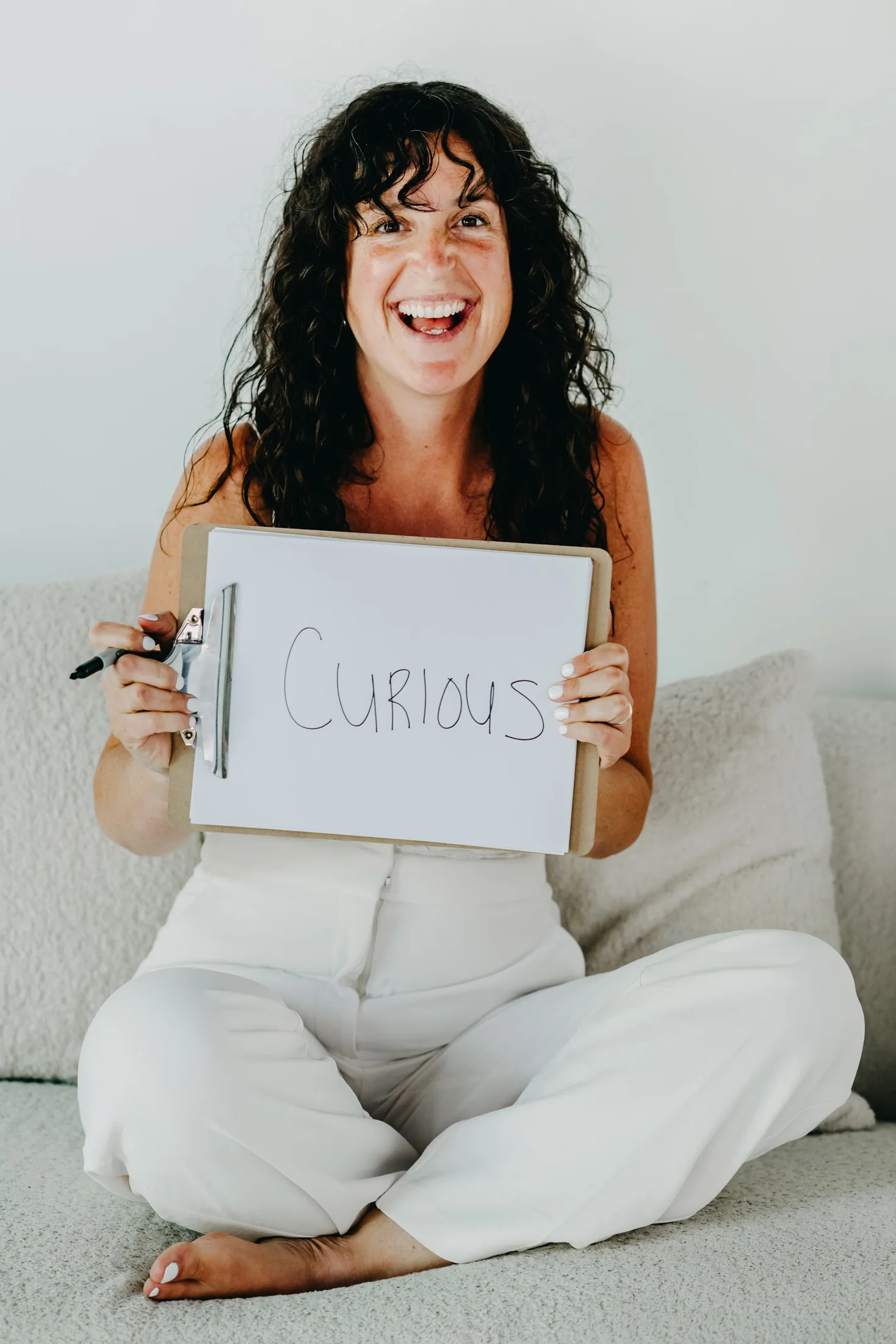 Shelby laughing while holding up a hand-lettered board that reads CURIOUS